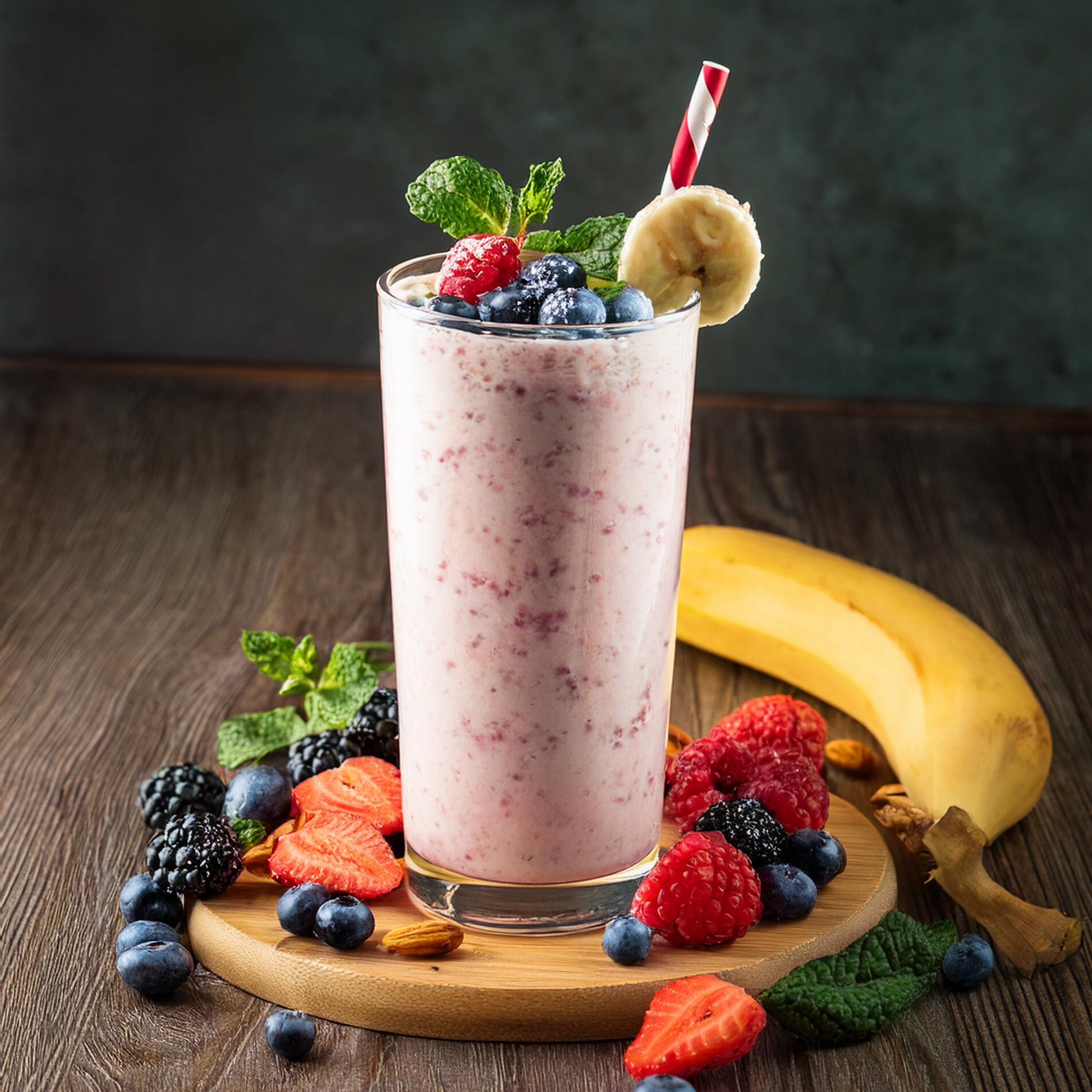 A tall glass of pink berry smoothie with cottage cheese, garnished with fresh berries, banana slices, and a mint sprig, set on a wooden counter.